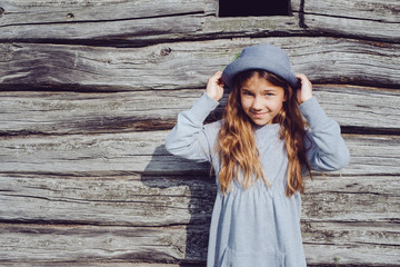 Joyful teen girl in casual clothes and blue hat posing by a wooden wall. Active lifestyle. Youth fashion