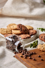 Roasted coffee beans get out of overturned glass jar on homespun tablecloth, selective focus, side view