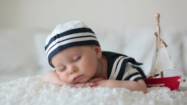 Cute baby boy, dressed in sailor clothes, sleeping with wooden boat