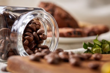Roasted coffee beans get out of overturned glass jar on homespun tablecloth, selective focus, side view