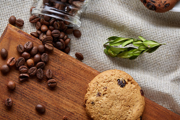 Fototapeta premium Roasted coffee beans get out of overturned glass jar on homespun tablecloth, selective focus, side view