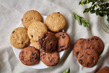 Side view of a plate of chocolate chip cookies on a white plate on homespun tablecloth, selective focus