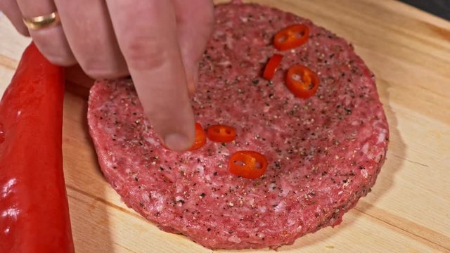 Cook makes meat medallions for burgers. Pouring spices pepper and salt. Meat marbled beef lies on food wooden board for cutting and red pepper chili. Chef in black food gloves makes cutlet medallion.