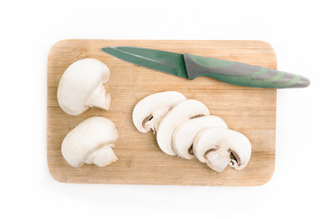 top view of sliced white mushrooms on a wooden board with a knife