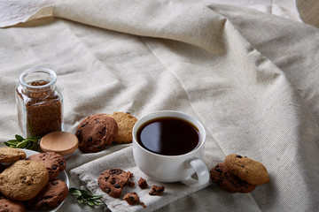 Morning coffee in white cup, chocolate chips cookies on cutting board close-up, selective focus