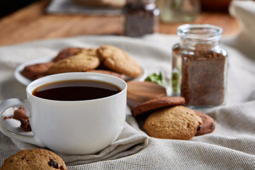 Morning coffee in white cup, chocolate chips cookies on cutting board close-up, selective focus