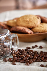 Roasted coffee beans get out of overturned glass jar on homespun tablecloth, selective focus, side view