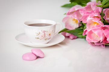Bouquet of tulips and cup of tea on white background. Holiday card. Soft focus, copy space. Spring concept.