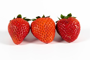 Drei reife Erdbeeren mit Grün isoliert auf weißem Hintergrund