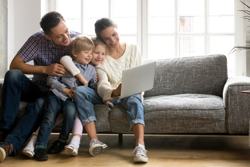 Happy family with little kids enjoying using application on laptop together, smiling parents...