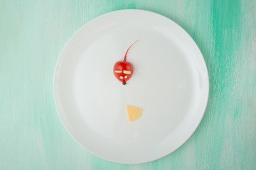 A mouse from a tomato and a slice of cheese, a creative from food on a white plate. The concept of eating.