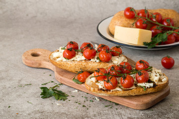 Open sandwiches with cheese, greens and fried cherry tomatoes on a old wooden board.