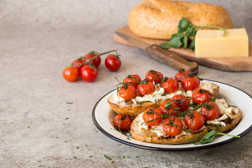 Open sandwiches with cheese, greens and fried cherry tomatoes on a round white plate.