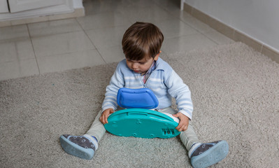 A little blond boy examines a toy, while sitting on the carpet in his room