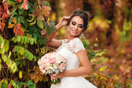 Portrait of beautiful bride standing near the trees in autumn forest