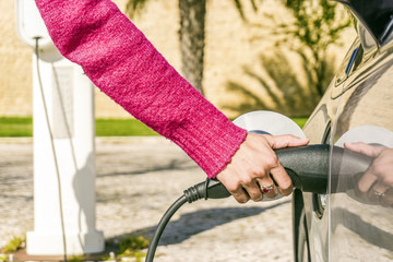 Obraz premium Woman plugs electric car to charging station