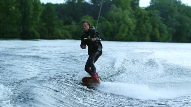 Athlete doing tricks on wakeboard. Young man wakeboarding on river wave. Wake boarding on city lake in slow motion. Male rider waterskiing. Extreme sports on city lake. Extreme lifestyle