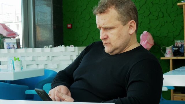 4k Middle age man siting alone in coffee house with mobile phone during business trip 