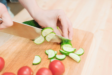 Obraz na płótnie Canvas close-up of female hands cut into fresh cut cucumbers on a wooden cutting board next to pink tomatoes. The concept of homemade vegetarian cuisine and healthy eating and lifestyle
