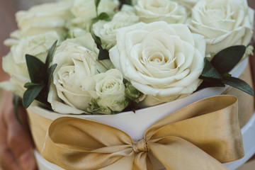 Rose box. Beautiful roses in white gift box with golden bow. Bride holding flower decoration on wedding day.