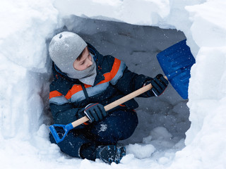 European boy is sitting in the snow cave and making it dipper.  - 200571683