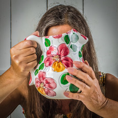 A middle-aged woman at home will hide behind a ceramic jug.