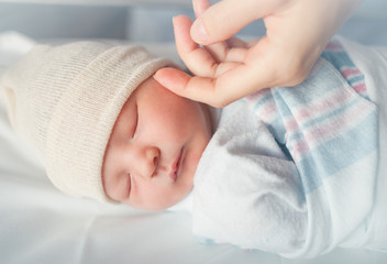 Little baby boy sleeping with mothers hand touching his soft skin.