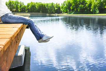 Female by lake siting on wooden dock. Chilling out in nature concept. - obrazy, fototapety, plakaty
