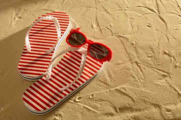 Naklejka premium Sandal and sunglasses on a sandy beach, sunset, top view