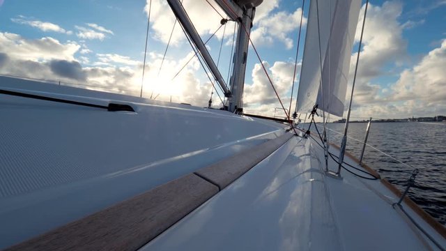 Slow motion. Yacht deck slowly rocking on the waves. Close up of the mast and sails of the yacht. Calm water surface, bright shining sun, blue clear sky, city or settlement. Great landscape of Norway