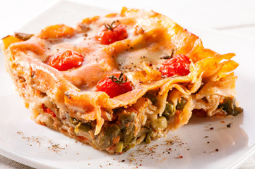 piece of lasagna close-up decorated with cherry tomatoes on white plate 