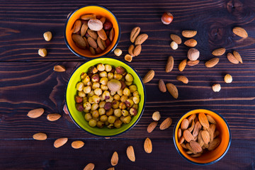 Different types of nuts: hazelnut and almonds, poured into colorful bowls on dark wooden background
