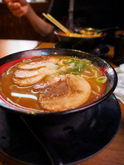 Close-up detail of a bowl of hot miso ramen topped with roasted chashu pork with customers eating in the background. Vertical orientation. Osaka, Japan. Travel and cuisine concept.