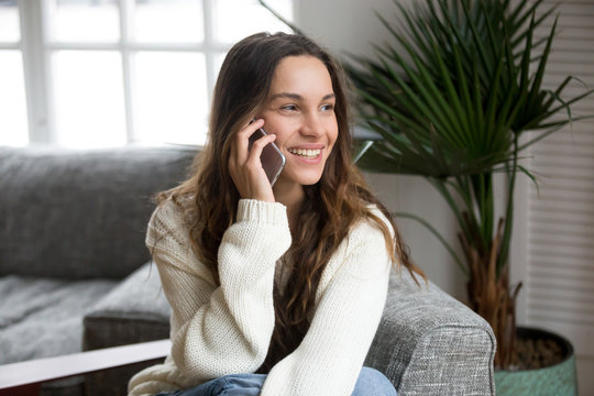 Smiling millennial mestizo woman talking on the phone at home, happy young girl holds cellphone making answering call, attractive teenager having pleasant conversation chatting by mobile with friend