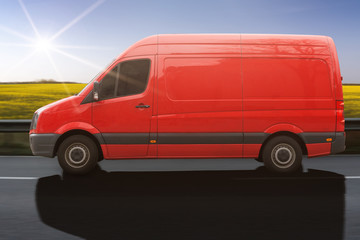 Obraz na płótnie Canvas roter Transporter fährt auf einer Landstraße an einem Rapsfeld vorbei