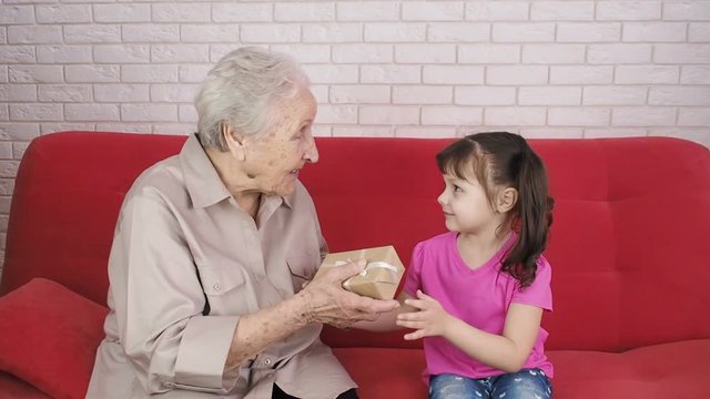 The child gives a gift. A little girl gives a gift to grandmother.