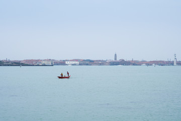 Venice, Italy: small arms boat with 2 rowers and the island of Murano in the background
