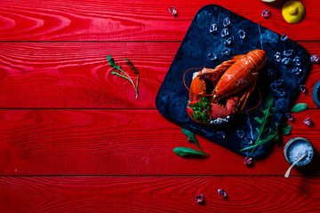 Portrait of a red lobster with a bouquet of parsley in a clove, small white snails grown on the lobsters shell, on a black stone tray on red wooden background, Valentines, Mothers day or Sorry Concept