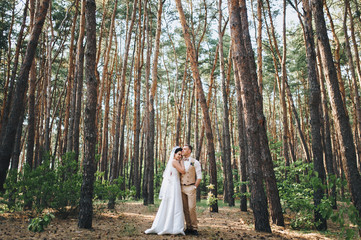 Beautiful newlyweds standing in the woods and hugging each other. Summer wedding. Stylish bride and groom outdoors.