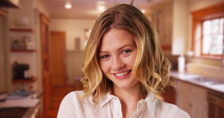 Attractive female with short blonde hair standing in kitchen smiling at camera