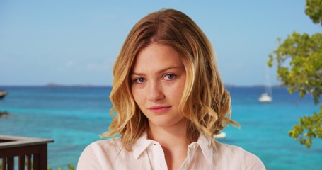 Female dressed in white button down looking confidently at camera with ocean