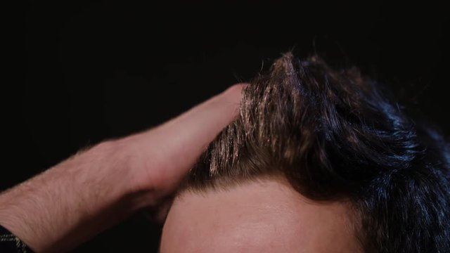 A young man touching his hair against a black background. Close-up macro shot