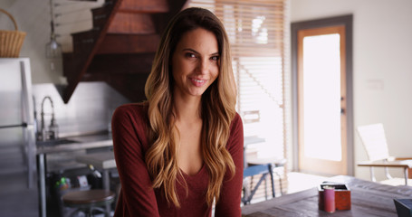 Attractive female millennial sitting inside kitchen smiling at camera