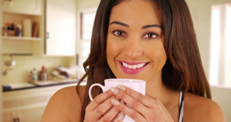 Close up of cheerful Latina female drinking from coffee mug inside kitchen