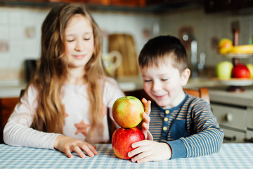Fototapeta premium Children eat apples in the kitchen at the morning. Sister and brother have fun. Kids build a tower of apples in the kitchen