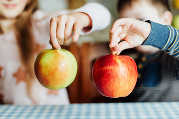 Children eat apples in the kitchen at the morning. The sister and brother hold the apple in their hands. Close-up