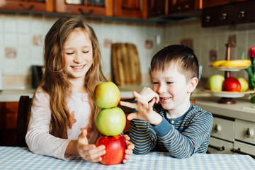 Children eat apples in the kitchen at the morning. Sister and brother have fun. Kids build a tower of apples in the kitchen