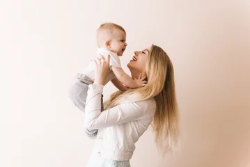 Fototapeten You are my treasure! cheerful beautiful young woman holding baby boy in her hands and looking at him with love  at home © ksyusha_yanovich