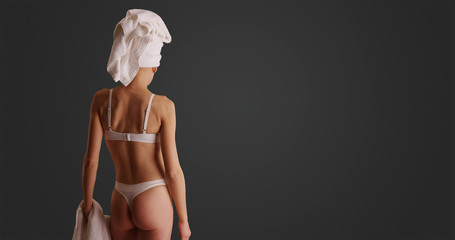 Rear view of woman in lingerie holding bath towel posing on grey background