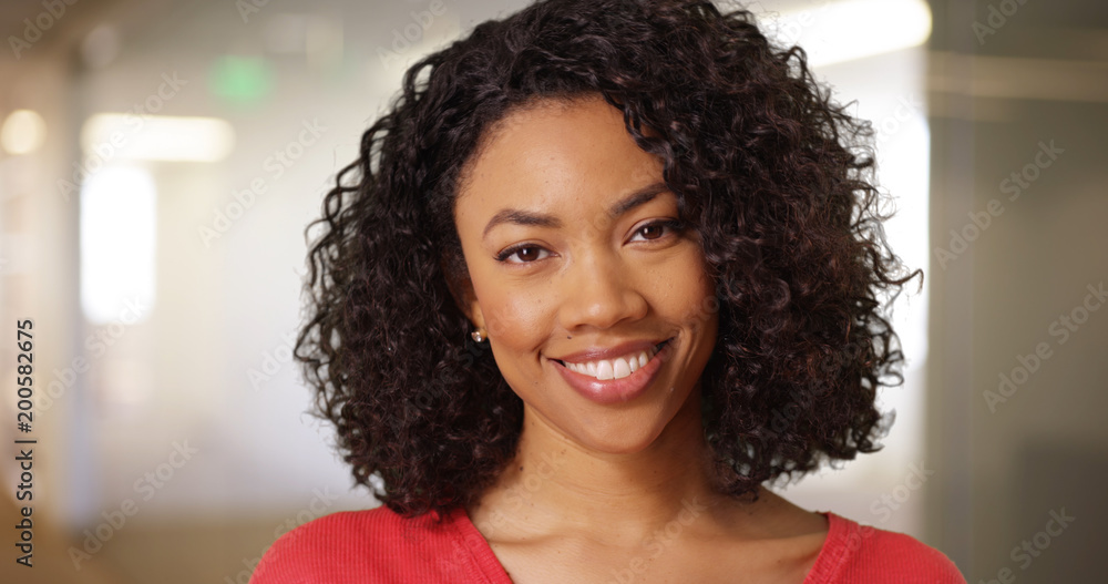 Wall mural Friendly young African lady with curly hair looking happily at camera indoors